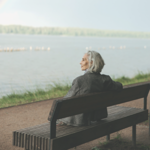A woman gazing out onto a lake while she is sat on a bench, depicting the area in which Sarah the Carer provides her personalised home care services.